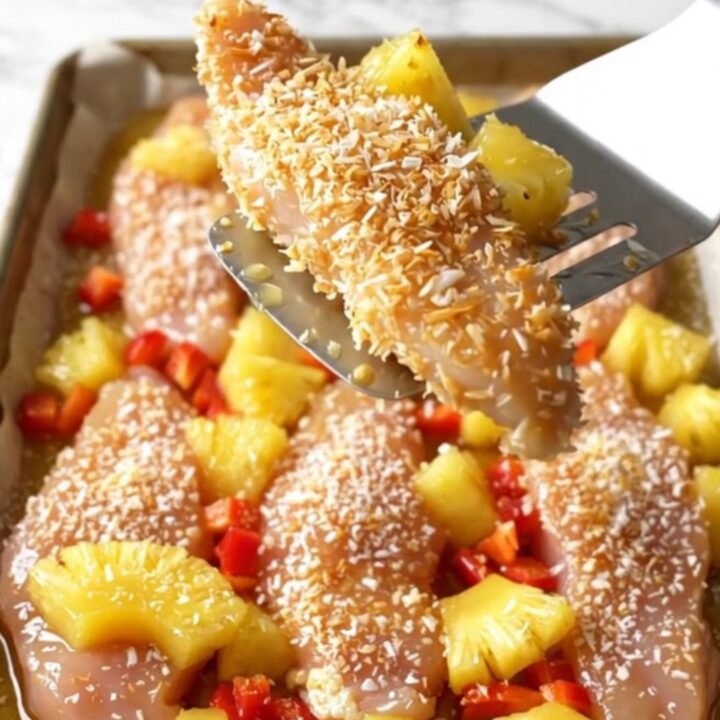 Crispy golden coconut chicken tenders on a sheet pan with roasted pineapple and red pepper chunks.