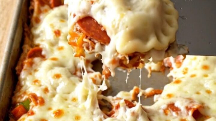 A golden, cheesy sheet pan filled with pepperoni pizza pierogies on a wooden background.
