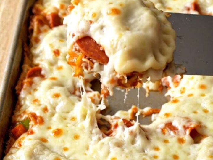 A golden, cheesy sheet pan filled with pepperoni pizza pierogies on a wooden background.