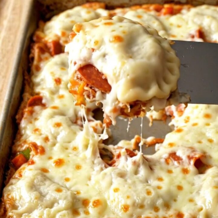 A golden, cheesy sheet pan filled with pepperoni pizza pierogies on a wooden background.