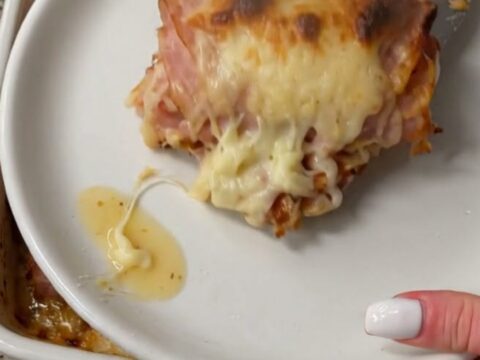 A spatula lifting a warm, cheesy ham roll from a baking dish, showcasing a long, stretchy cheese pull.