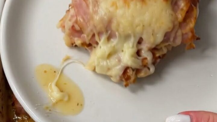 A spatula lifting a warm, cheesy ham roll from a baking dish, showcasing a long, stretchy cheese pull.