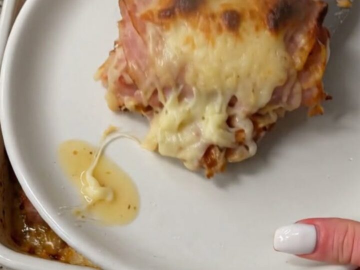 A spatula lifting a warm, cheesy ham roll from a baking dish, showcasing a long, stretchy cheese pull.