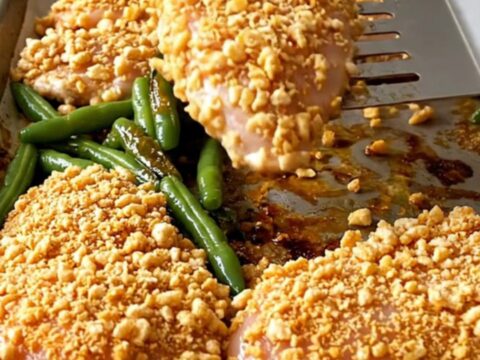 A golden, crispy cereal-crusted chicken breast served with blistered green beans on a parchment-lined sheet pan.