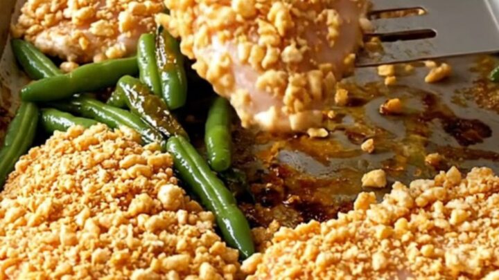 A golden, crispy cereal-crusted chicken breast served with blistered green beans on a parchment-lined sheet pan.