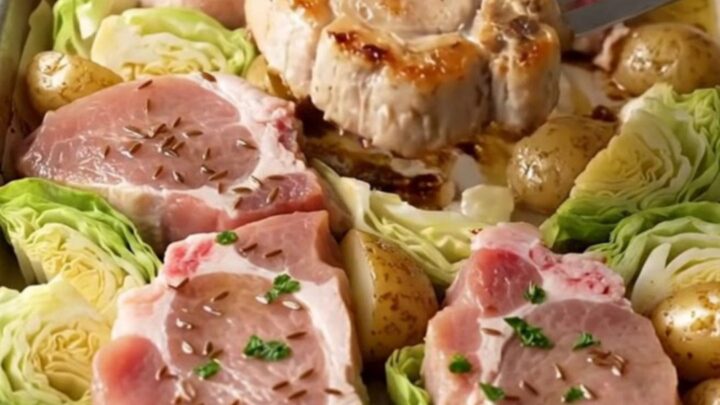 A sheet pan filled with golden-brown roasted pork chops, tender cabbage wedges, and roasted baby potatoes.