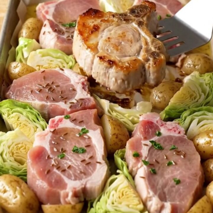 A sheet pan filled with golden-brown roasted pork chops, tender cabbage wedges, and roasted baby potatoes.