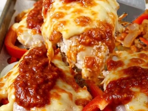 A sheet pan filled with golden-brown chicken breasts topped with melted mozzarella and tomato sauce