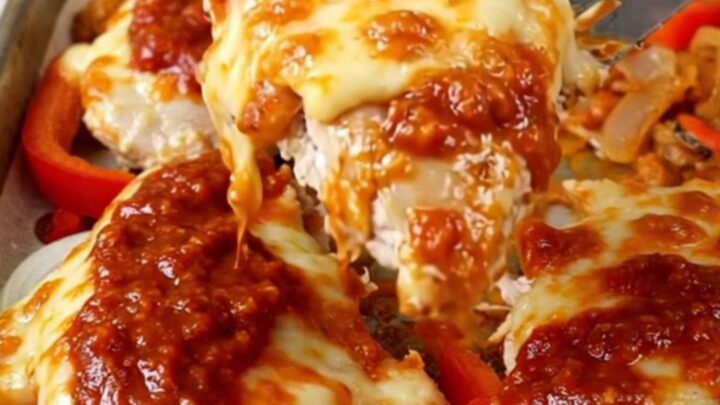 A sheet pan filled with golden-brown chicken breasts topped with melted mozzarella and tomato sauce