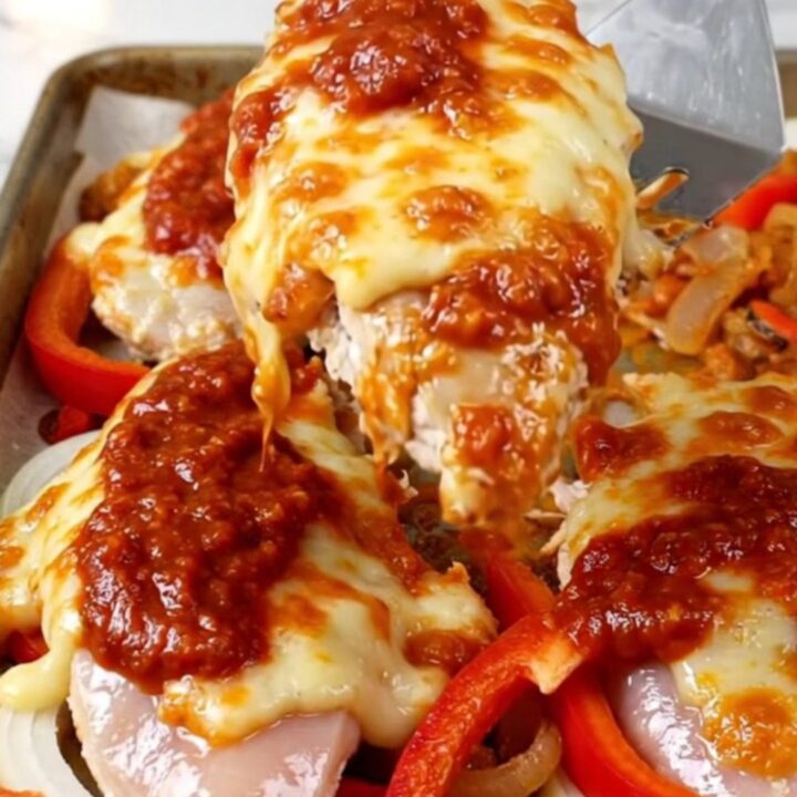 A sheet pan filled with golden-brown chicken breasts topped with melted mozzarella and tomato sauce