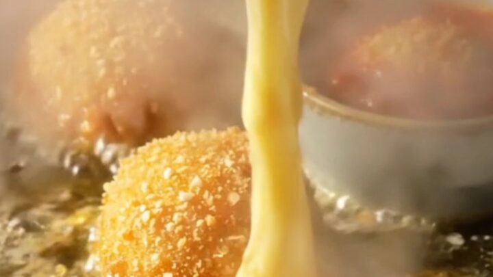 A close-up shot of a golden, crispy potato croquette being pulled apart to reveal a long, stringy mozzarella cheese pull.