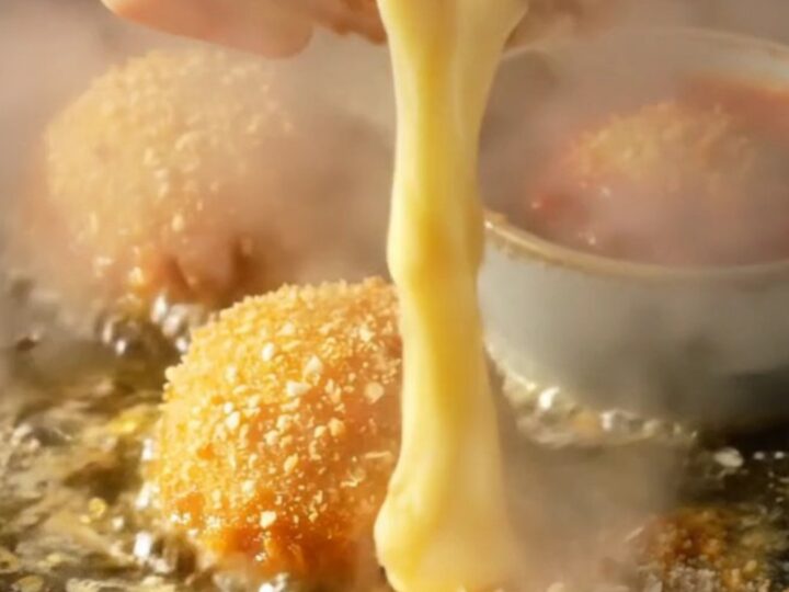 A close-up shot of a golden, crispy potato croquette being pulled apart to reveal a long, stringy mozzarella cheese pull.