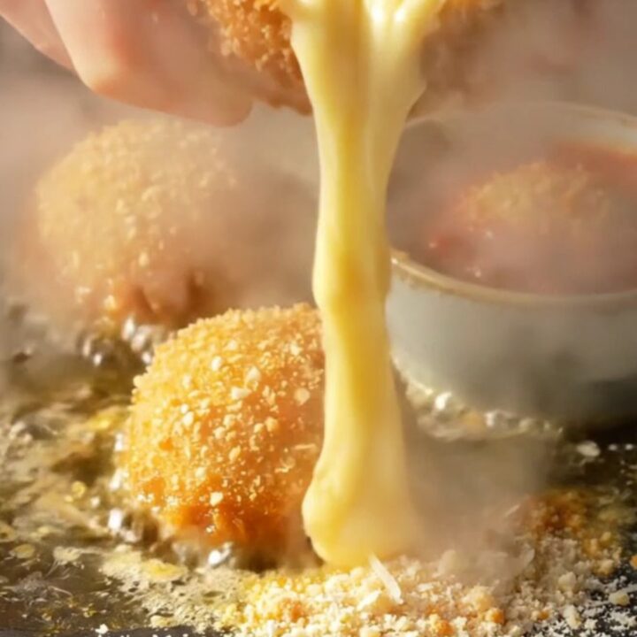 A close-up shot of a golden, crispy potato croquette being pulled apart to reveal a long, stringy mozzarella cheese pull.
