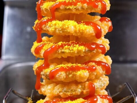 A crispy golden tornado spiral potato on a bamboo skewer, dusted with seasoning and drizzled with spicy mayo.