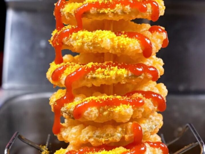 A crispy golden tornado spiral potato on a bamboo skewer, dusted with seasoning and drizzled with spicy mayo.