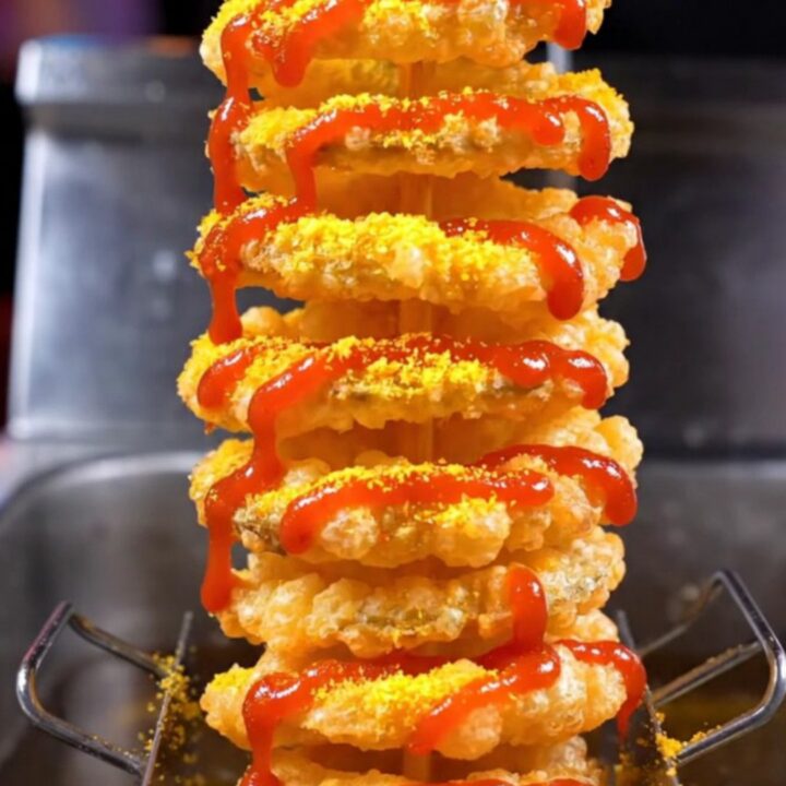 A crispy golden tornado spiral potato on a bamboo skewer, dusted with seasoning and drizzled with spicy mayo.