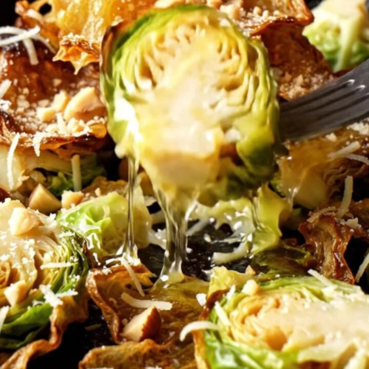 Crispy smashed Brussels sprouts drizzled with hot honey and topped with hazelnuts on a rustic plate.