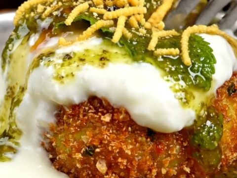 A close-up of a golden, crispy stuffed Aloo Tikki with a crack in the crust revealing a steaming pea and paneer filling.