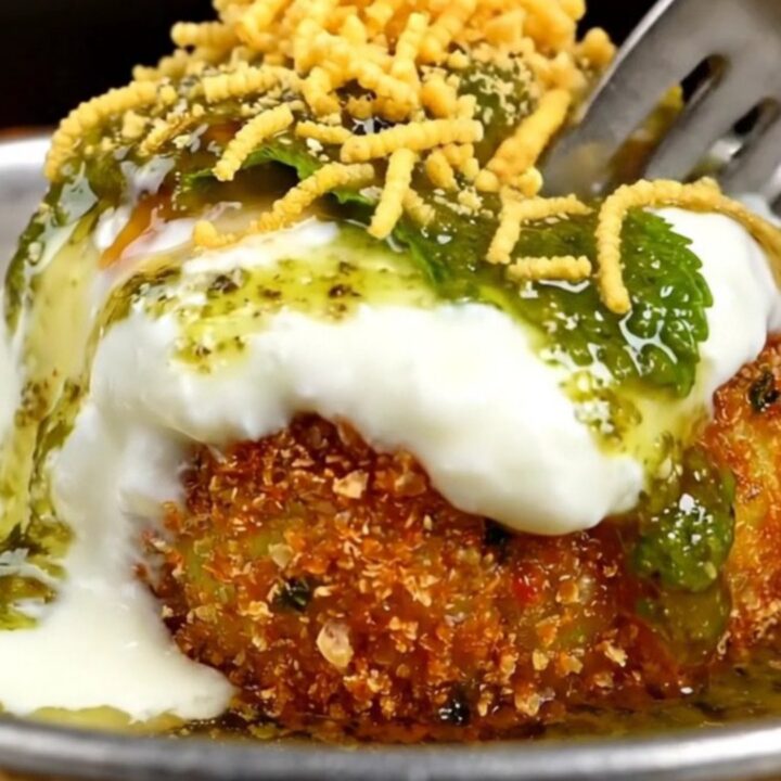 A close-up of a golden, crispy stuffed Aloo Tikki with a crack in the crust revealing a steaming pea and paneer filling.