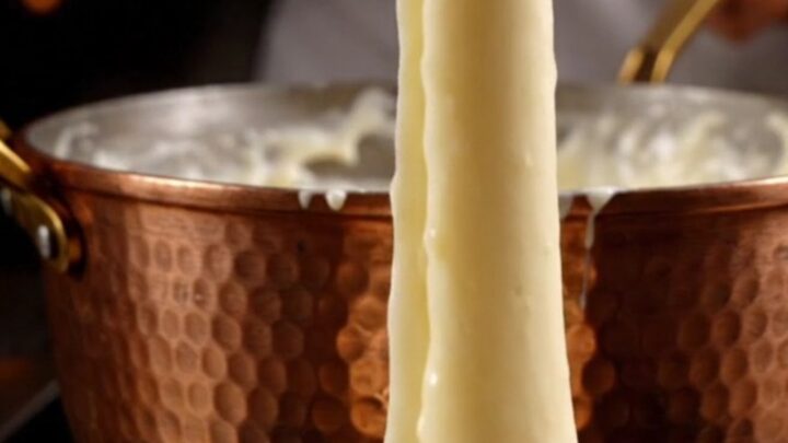 A wooden spoon lifting a long, glossy, elastic ribbon of French Aligot from a copper pot.