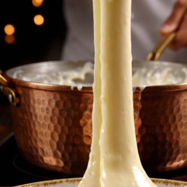 A wooden spoon lifting a long, glossy, elastic ribbon of French Aligot from a copper pot.