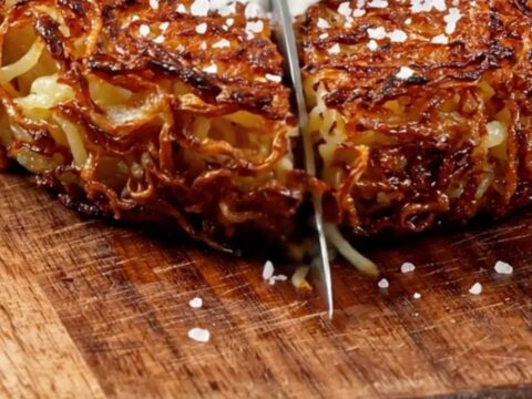 A crispy, golden-brown Swiss potato rösti served on a wooden board with sour cream and chives.