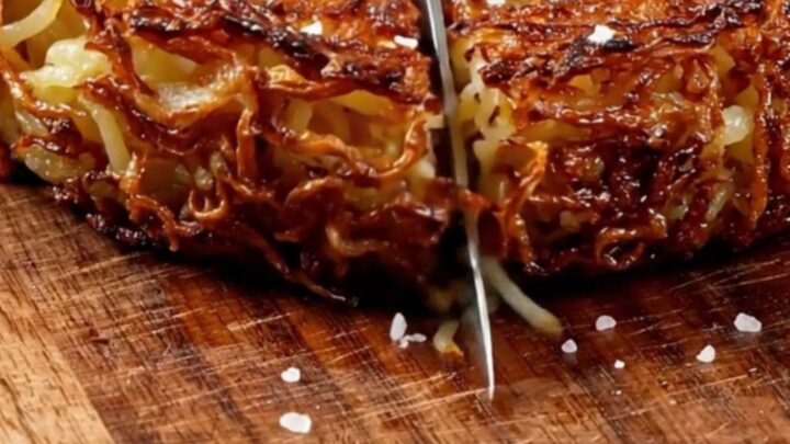 A crispy, golden-brown Swiss potato rösti served on a wooden board with sour cream and chives.
