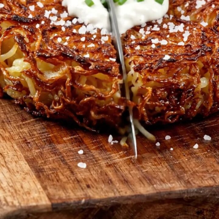 A crispy, golden-brown Swiss potato rösti served on a wooden board with sour cream and chives.