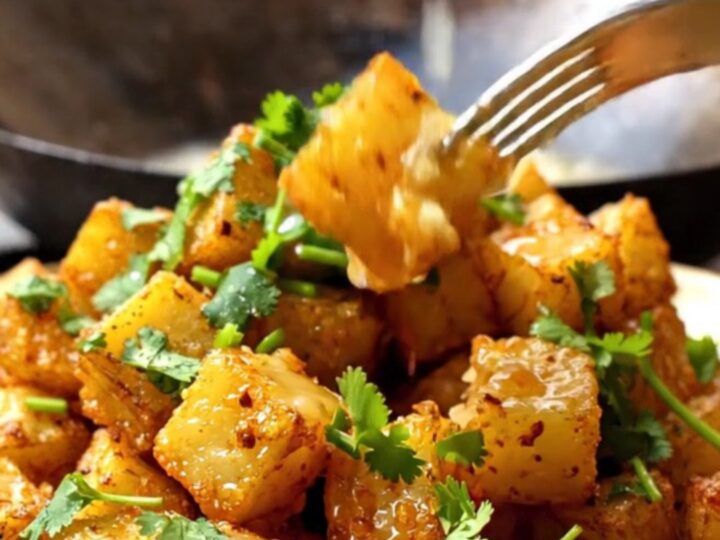 A close-up of golden-fried Batata Harra potatoes in a rustic bowl, garnished with fresh cilantro and lemon.