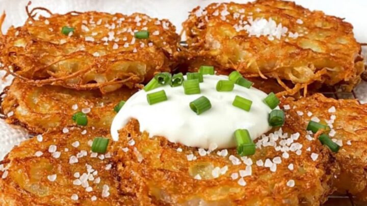 A stack of golden-brown, lacy potato latkes topped with cool sour cream and fresh green chives.