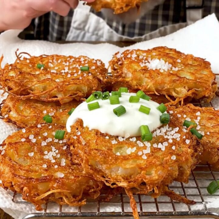 A stack of golden-brown, lacy potato latkes topped with cool sour cream and fresh green chives.