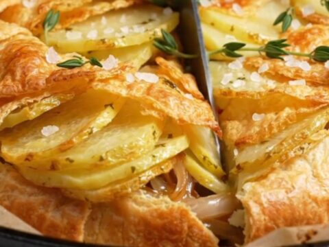 A golden, crispy potato galette inverted onto a white platter, showing beautiful overlapping potato shingles.