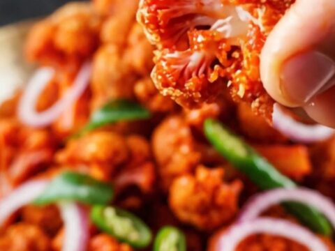 A vibrant bowl of crispy golden-brown Gobi 65 topped with fresh lime wedges and sliced onion rings.