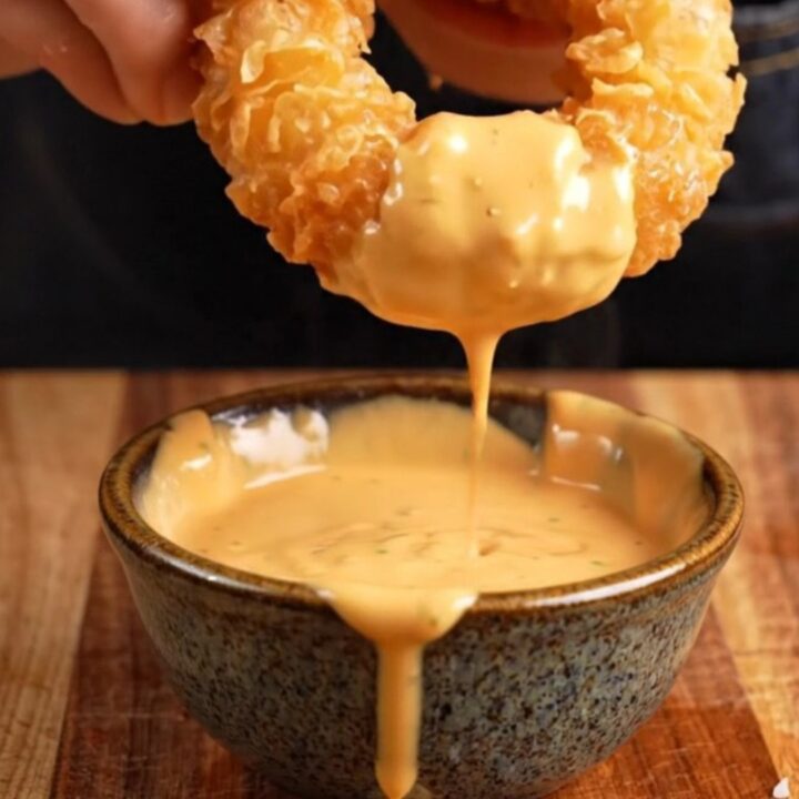 A close-up of a crispy beer-battered onion ring being pulled apart to reveal the sweet, tender onion inside.