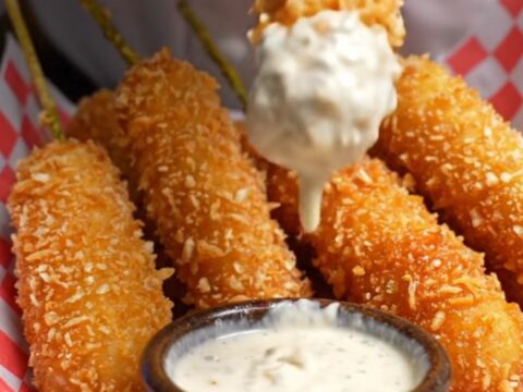 A golden, panko-crusted fried pickle spear being pulled in half, showing a crunchy exterior and a juicy dill center.