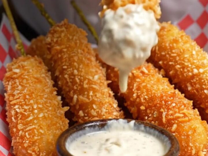 A golden, panko-crusted fried pickle spear being pulled in half, showing a crunchy exterior and a juicy dill center.
