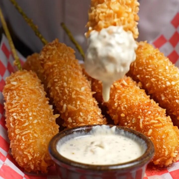 A golden, panko-crusted fried pickle spear being pulled in half, showing a crunchy exterior and a juicy dill center.