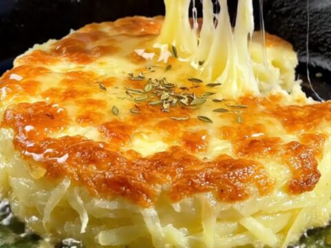 A crispy golden-brown potato and cheese cake in a cast-iron skillet, drizzled with honey and lemon.