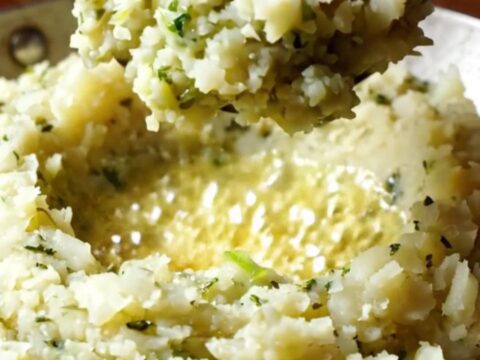 A close-up of a steaming bowl of Irish Colcannon with a well of sizzling brown butter in the center.