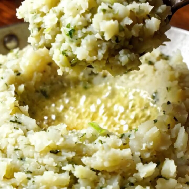 A close-up of a steaming bowl of Irish Colcannon with a well of sizzling brown butter in the center.