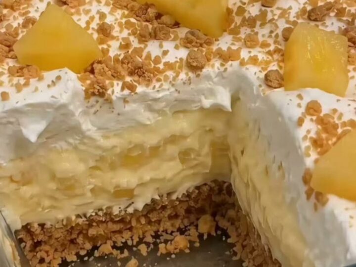Layered no-bake pineapple cream dessert in a glass baking dish with a metal spoon scooping out a generous portion.