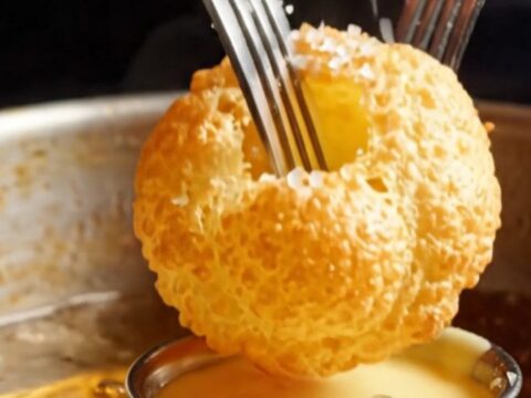 Golden, perfectly puffed hollow potato pillows arranged on a white plate with a side of creamy bearnaise sauce.