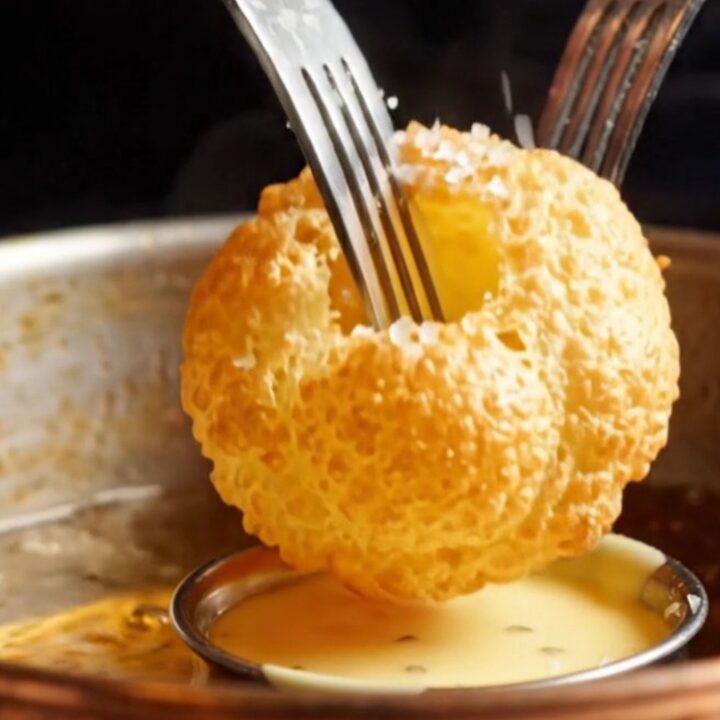 Golden, perfectly puffed hollow potato pillows arranged on a white plate with a side of creamy bearnaise sauce.