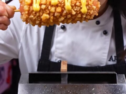 A close-up shot of a Korean potato-crusted mozzarella corn dog being pulled apart, revealing a long, stretchy cheese core.