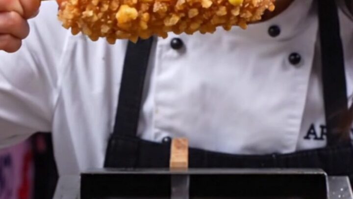 A close-up shot of a Korean potato-crusted mozzarella corn dog being pulled apart, revealing a long, stretchy cheese core.