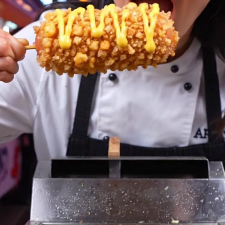 A close-up shot of a Korean potato-crusted mozzarella corn dog being pulled apart, revealing a long, stretchy cheese core.