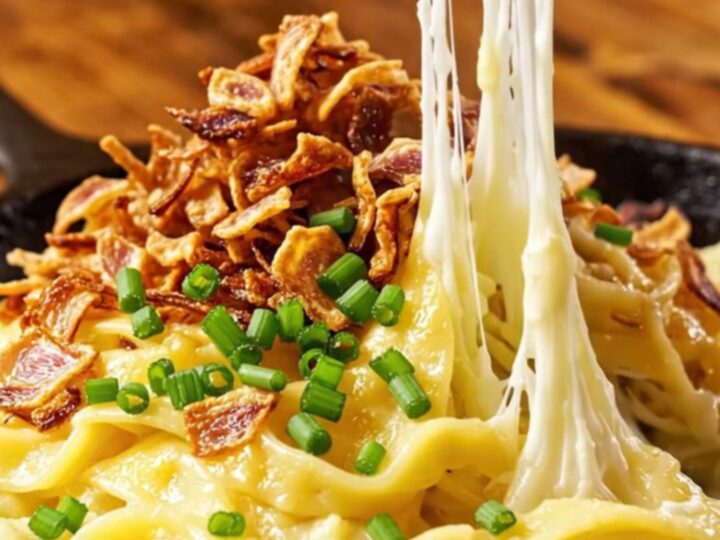 A steaming, golden-brown portion of Käsespätzle topped with crispy shallots and fresh chives.