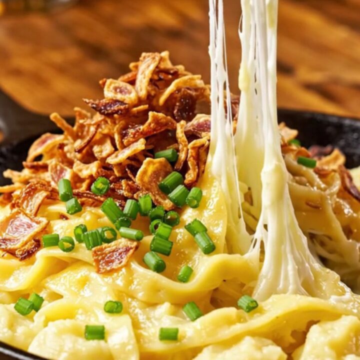 A steaming, golden-brown portion of Käsespätzle topped with crispy shallots and fresh chives.