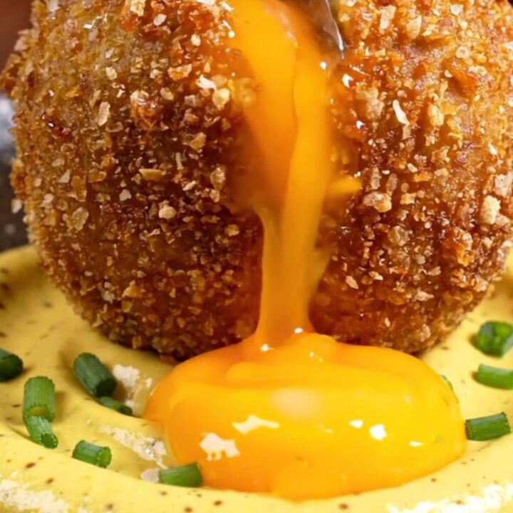 A golden-fried Scotch-style potato bomb sliced in half, revealing a perfectly jammy, molten orange egg yolk flowing out.