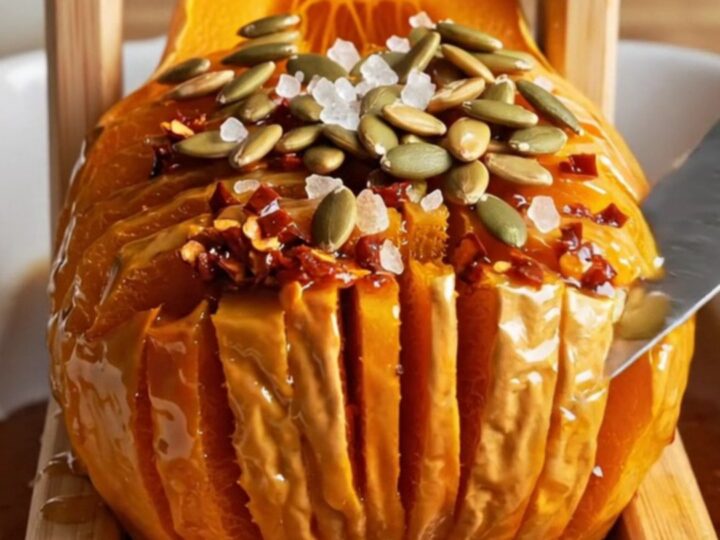 A golden, caramelized hasselback butternut squash half garnished with toasted pepitas on a rustic stoneware plate.